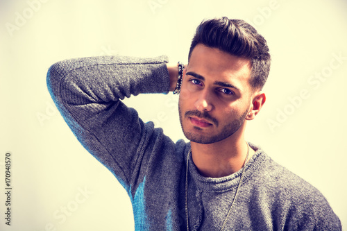 Handsome young man wearing grey sweater and ripped jeans, on light background in studio shot © theartofphoto