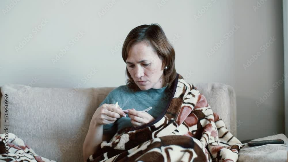 A woman puts herself an electronic thermometer under her arm. A sick woman measures body temperature. A woman puts herself an electronic thermometer under her arm. A sick woman measures body temperature.