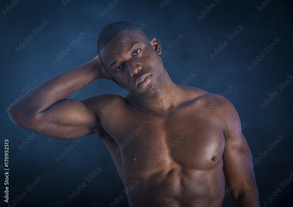 Handsome shirtless muscular black young man, looking at camera, on dark background in studio shot Handsome shirtless muscular black young man, looking at camera, on dark background in studio shot