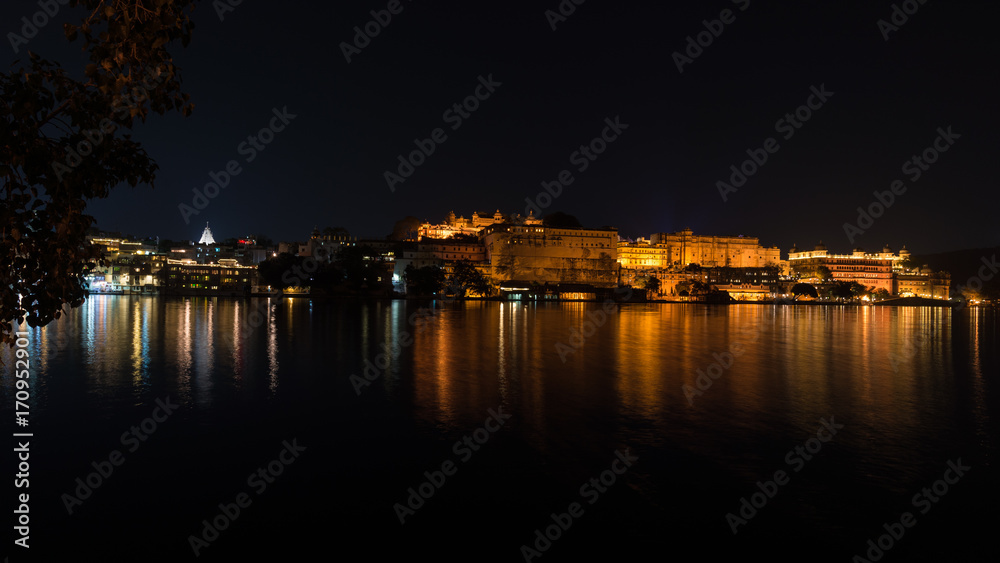 Udaipur cityscape by night. The majestic city palace reflecting lights on Lake Pichola, travel destination in Rajasthan, India.