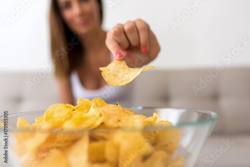 A young beautiful Woman relaxing on a sofa having potato Chips  