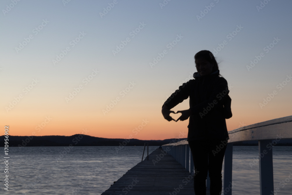 Girl on a pier making heart sillhouette at sunset