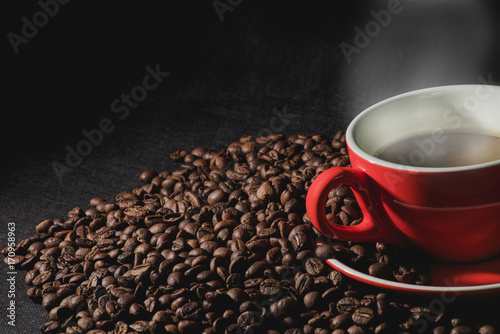 Hot coffee in red cup and coffee beans are the background.