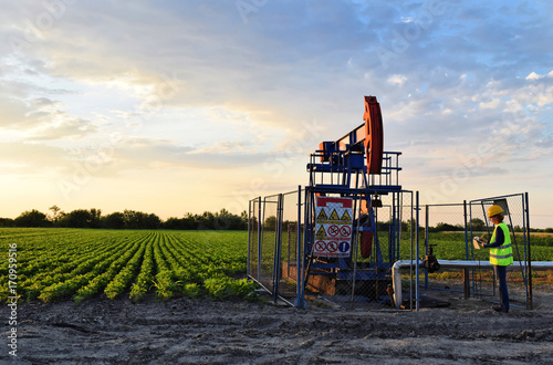 A female engineer at work on an European oil well during dusk time, agriculture field in background    