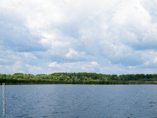 Beautiful landscape of a lake and bulrush greenery, dynamic sky with white clouds © watcherfox