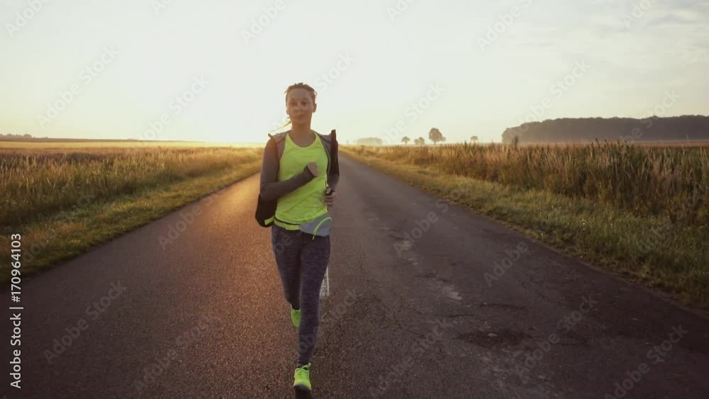 Woman Running on a Countryside Road at Sunrise. Steadicam STABILIZED shot, SLOW MOTION 120 fps. Female jogger athlete training at dusk. Active healthy lifestyle concept. Cinematic sports shot. Woman Running on a Countryside Road at Sunrise. Steadicam STABILIZED shot, SLOW MOTION 120 fps. Female jogger athlete training at dusk. Active healthy lifestyle concept. Cinematic sports shot.