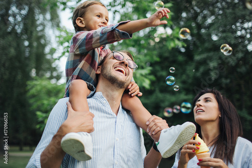 Happy young family playing with bubble wands in park outdoors