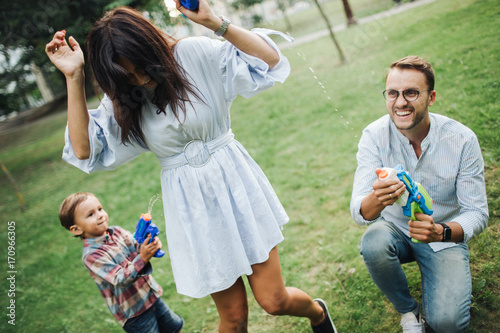 Baby boy playing water guns with young parents in park