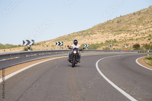 Young man riding a motorcycle on road in a curve in the mountains on sunny day.