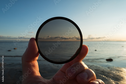 Man holding gradient neutral density ND filter on background of summer sunset photo