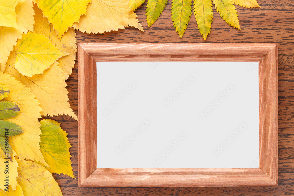 A wooden frame for photos lies on a table among the yellow autumn leaves.
