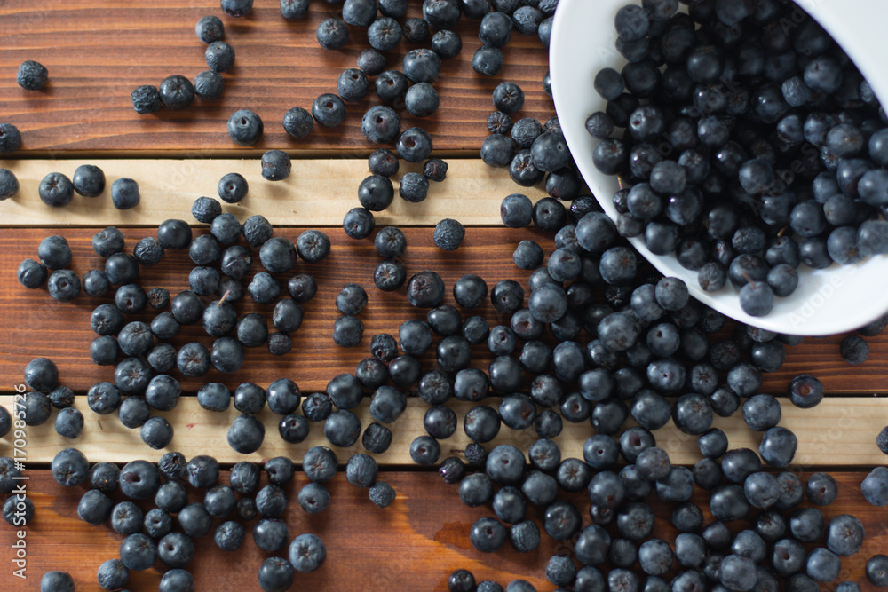Bowl full of aronia spilled on wooden table Bowl full of aronia spilled on wooden table