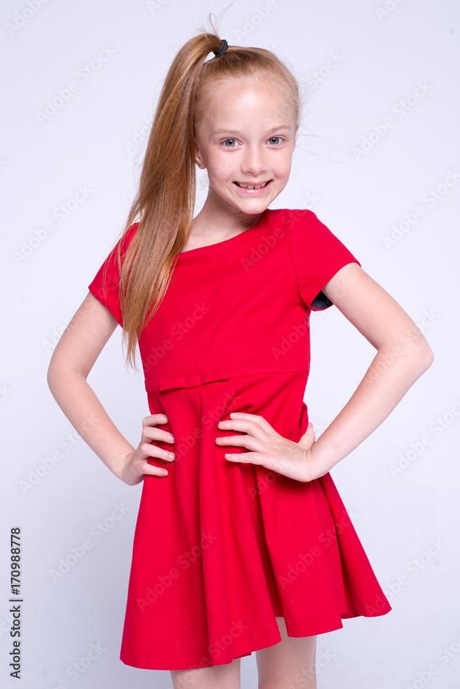 Beautiful little redhead girl in red dress posing like model on white background. Beautiful little redhead girl in red dress posing like model on white background.