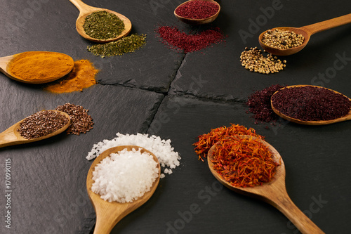 Colorful indian spices in wooden spoons on dark stone background