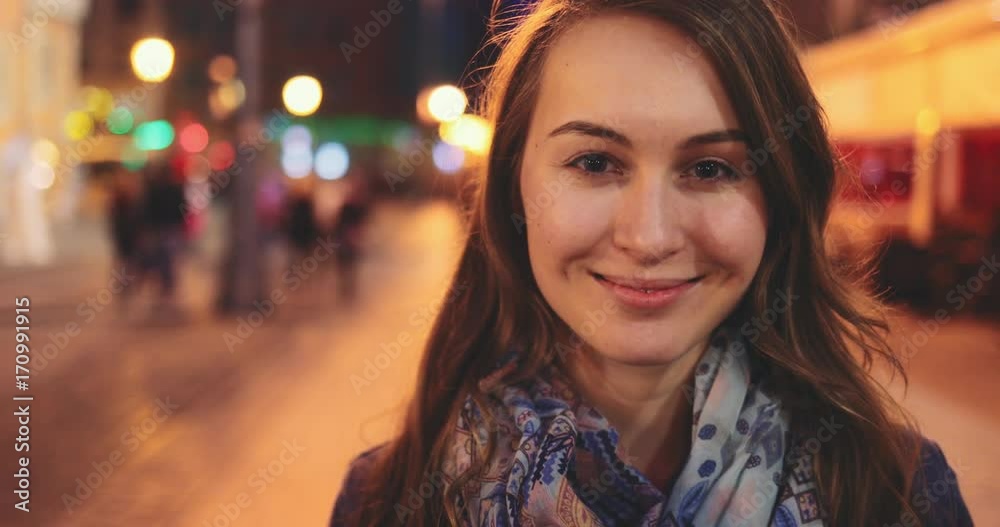 Portrait of a Beautiful Young Woman at Night in the City. SLOW MOTION 4K DCi. Attractive Happy Girl looking to camera. Blurred Night Busy Street lights background. Portrait of a Beautiful Young Woman at Night in the City. SLOW MOTION 4K DCi. Attractive Happy Girl looking to camera. Blurred Night Busy Street lights background.