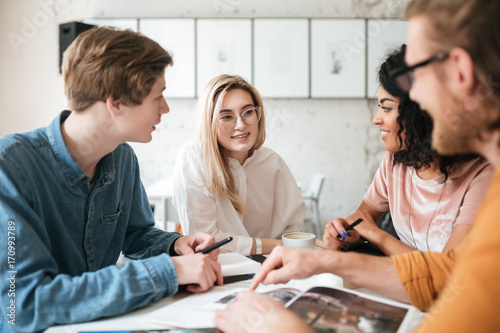 Portrait of young people sitting in office and happily looking at each other while discussion something. Group of cool guys working on new project in office. Young students creating something new photo