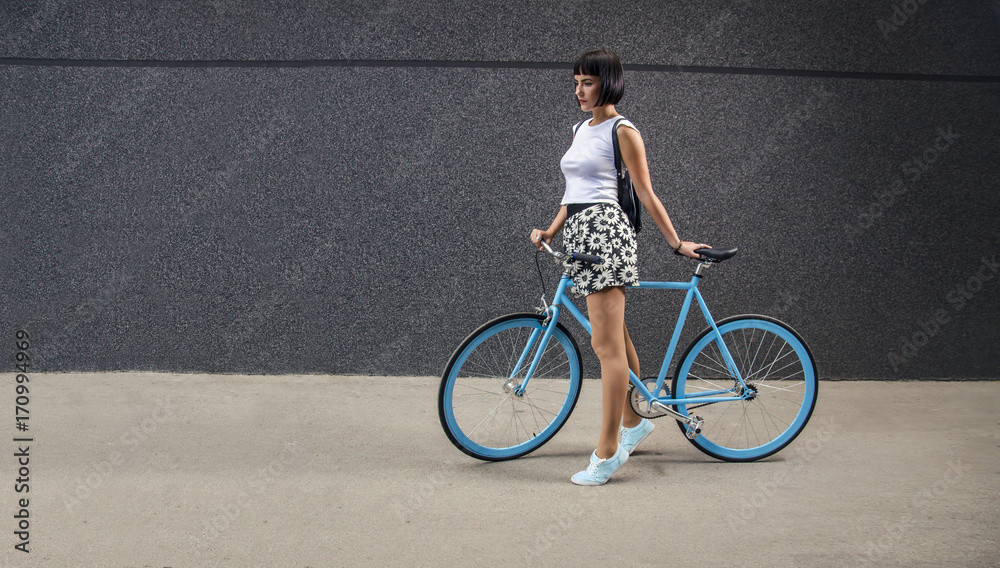 Obraz premium Urban hipster girl with all blue bicycle next to modern wall, copy space 