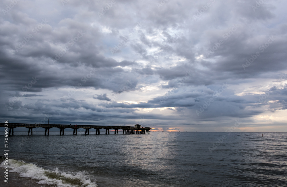 storm clouds rolling in over an ocean fishing pier at sunrise