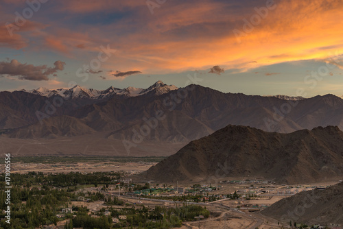 dramatic colorful sunset with mountains cover with snow and small city below Dramatic overcast sky. Leh, Ladakh, India.  Everest rang mountains. Beauty world.