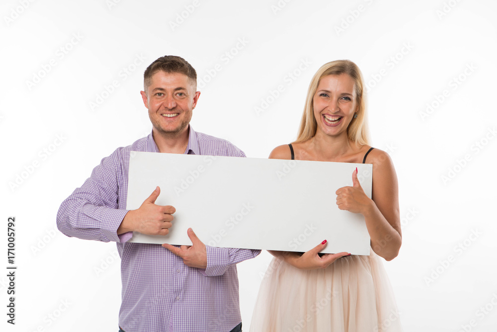 Young happy couple portrait of a confident businessman showing presentation, pointing placard gray background. Ideal for banners, registration forms, presentation, landings, presenting concept. Young happy couple portrait of a confident businessman showing presentation, pointing placard gray background. Ideal for banners, registration forms, presentation, landings, presenting concept.