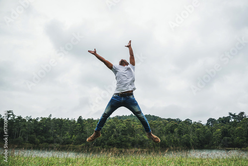Asian man travel relax in the holiday. Jump on a green pasture.