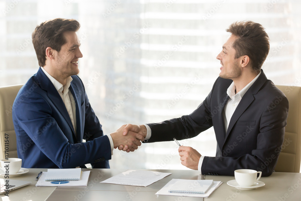 Happy smiling business partners shaking hands and congratulating each other after singing contract, successful negotiations, profitable partnership, trust between company leaders, conclusion agreement Happy smiling business partners shaking hands and congratulating each other after singing contract, successful negotiations, profitable partnership, trust between company leaders, conclusion agreement