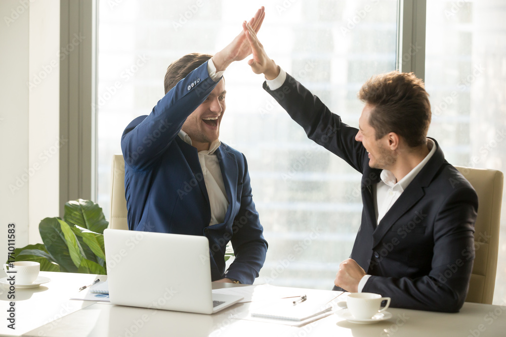 Φωτογραφία Excited businessman smiling and giving high five to his business partner or colleague while sitting at meeting table in office