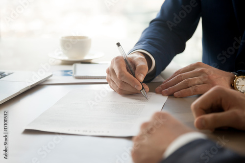 Close up image of businessman hand putting personal signature on contract document in presence of business partner. Starting successful partnership with entrepreneur or companie, making good deal photo