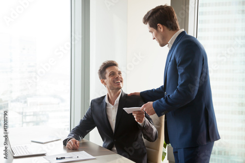 General manager presenting an envelope with premium or bonus cash to male company official. Boss congratulating happy employee with career promotion, thanking for good job and giving financial reward photo