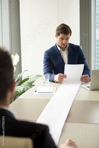 Executive recruiter looking surprised when reading applicants resume, shocked with long list of achievements, experiences and recommendations of job candidate, confused because of strange items in CV