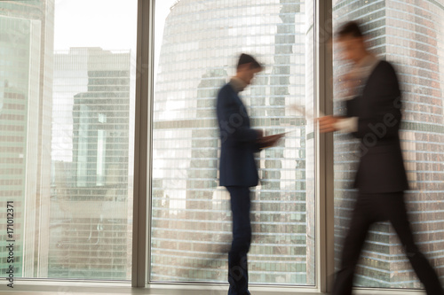 Foto Image of blurry silhouettes of office workers hurrying in business past large window with city view in modern office