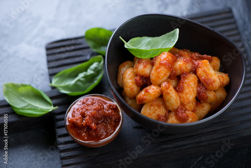 Bowl of potato gnocchi with red pesto sauce and green basil leaves, selective focus, studio shot