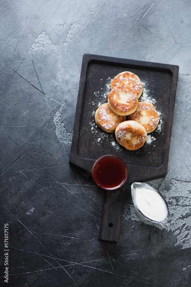 Φωτογραφία Cottage cheese pancakes or syrniki with sour cream and jam on a black wooden serving tray