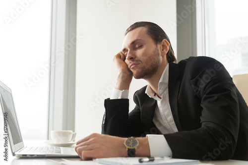 Photos Young businessman dozed in front of laptop in office
