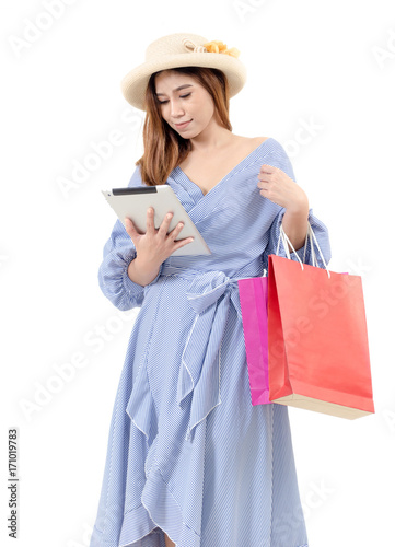 beautiful asian young woman with hat holding shopping bags and watching special offer in her tablet isolated on white background, online shopping, sale season, lifestyle technology concept, soft focus