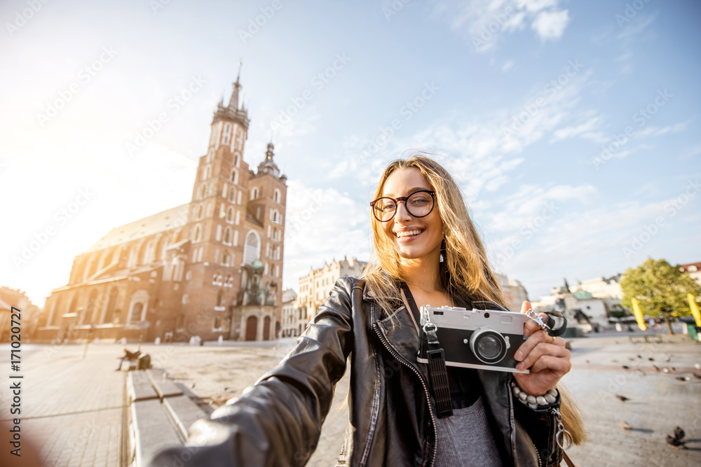 Portrait of a young stylish woman tourist in front of the famous St. Mary's Basilica on the Market square during the sunrise in Krakow, Poland