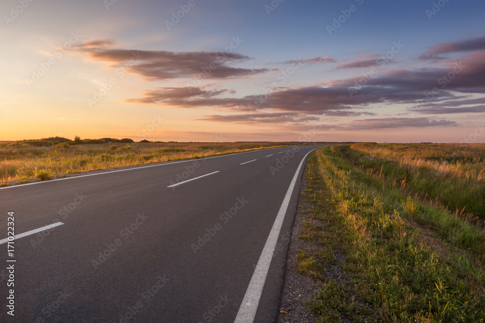 Curved asphalt road in plain at idyllic sunset