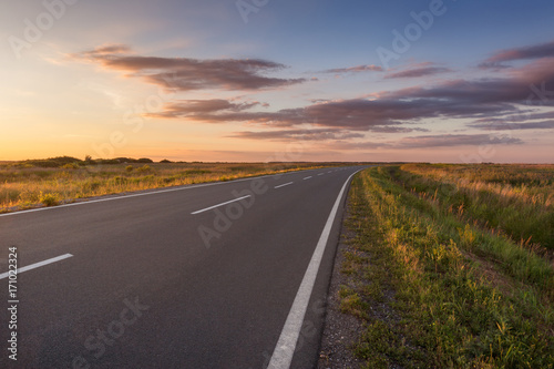Curved asphalt road in plain at idyllic sunset