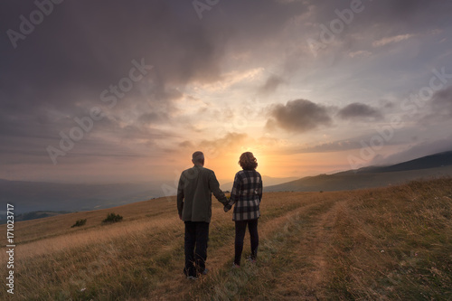 Senior couple hold hands on hill at idyllic sunset
