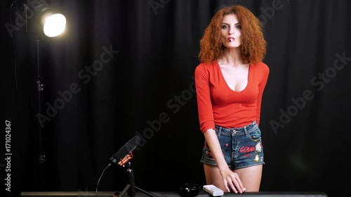 Skinny girl with wild red hair loves smoking a 120mm. Wearing a red low-cut top and cute jeans shorts.