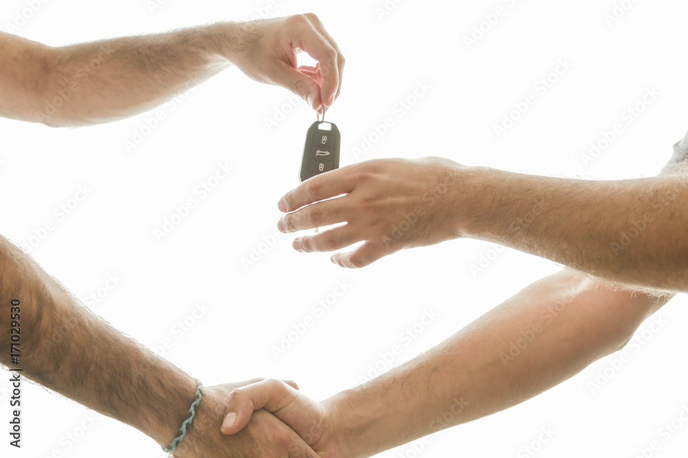 Car salesman handing over the keys for a new car to a young businessman . Handshake between two business people. Focus on a key. sales and handshake isolated on white background Car salesman handing over the keys for a new car to a young businessman . Handshake between two business people. Focus on a key. sales and handshake isolated on white background