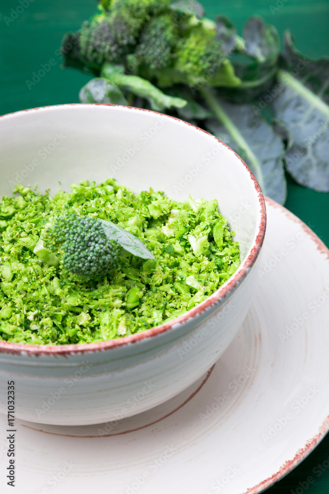 Broccoli rice in bowl on green background. Top view. Overhead. Copy space. Shredded broccoli. Broccoli rice in bowl on green background. Top view. Overhead. Copy space. Shredded broccoli.