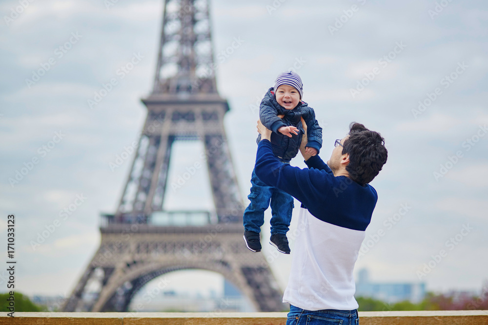Fototapeta premium Ojciec wyrzucający swojego małego synka w powietrze w pobliżu wieży Eiffla