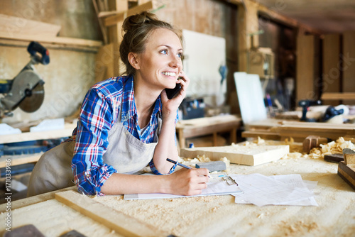 Bild auf Leinwand Cheerful young carpenter discussing order details with her customer on smartphon
