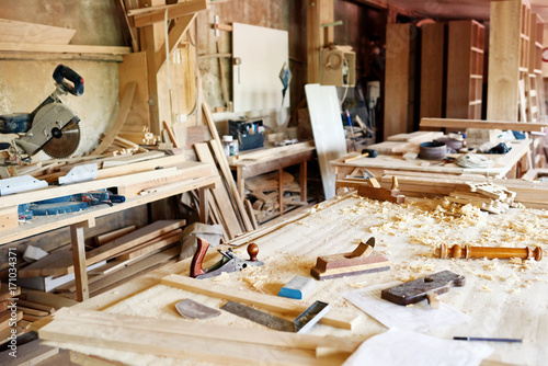 Schilderij op canvas Interior of spacious messy workshop: table with wooden planks, woodworking tools