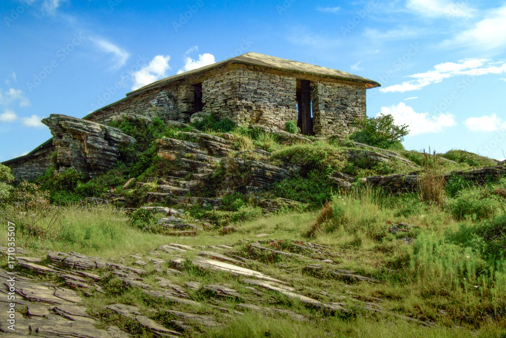 Solitary hut in the woods. Stone cabin on the top of a mountain. Blue sky background