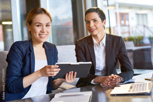 Group portrait of attractive white collar workers looking at camera with toothy smiles while having working meeting at cozy small coffeehouse with panoramic windows