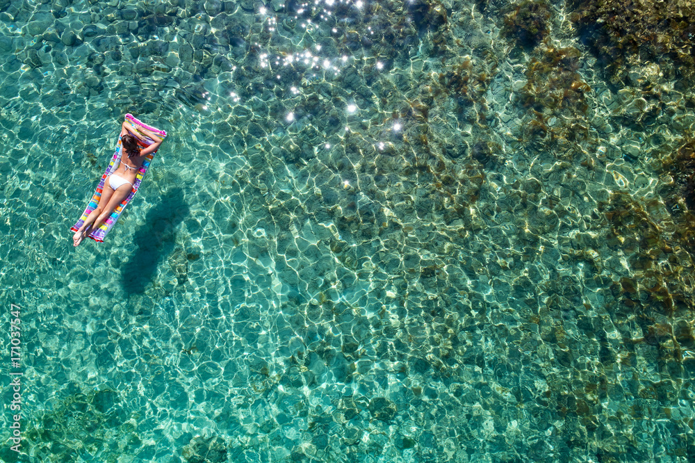 aerial view of a beautiful young woman in bikini on a matress in the sea