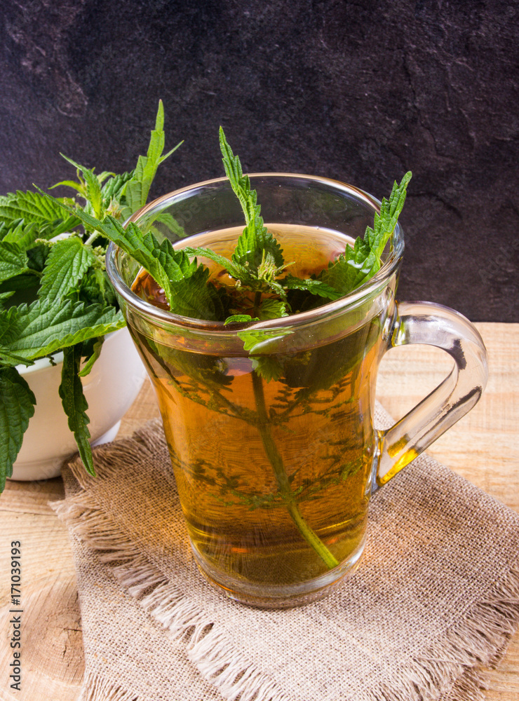 Healing tea with nettle. Tea in a glass cup on a wooden table. The source of vitamins. Healing tea with nettle. Tea in a glass cup on a wooden table. The source of vitamins.
