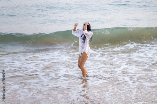 Chica joven con camisa blanca jugando con las olas en el mar al atardecer.